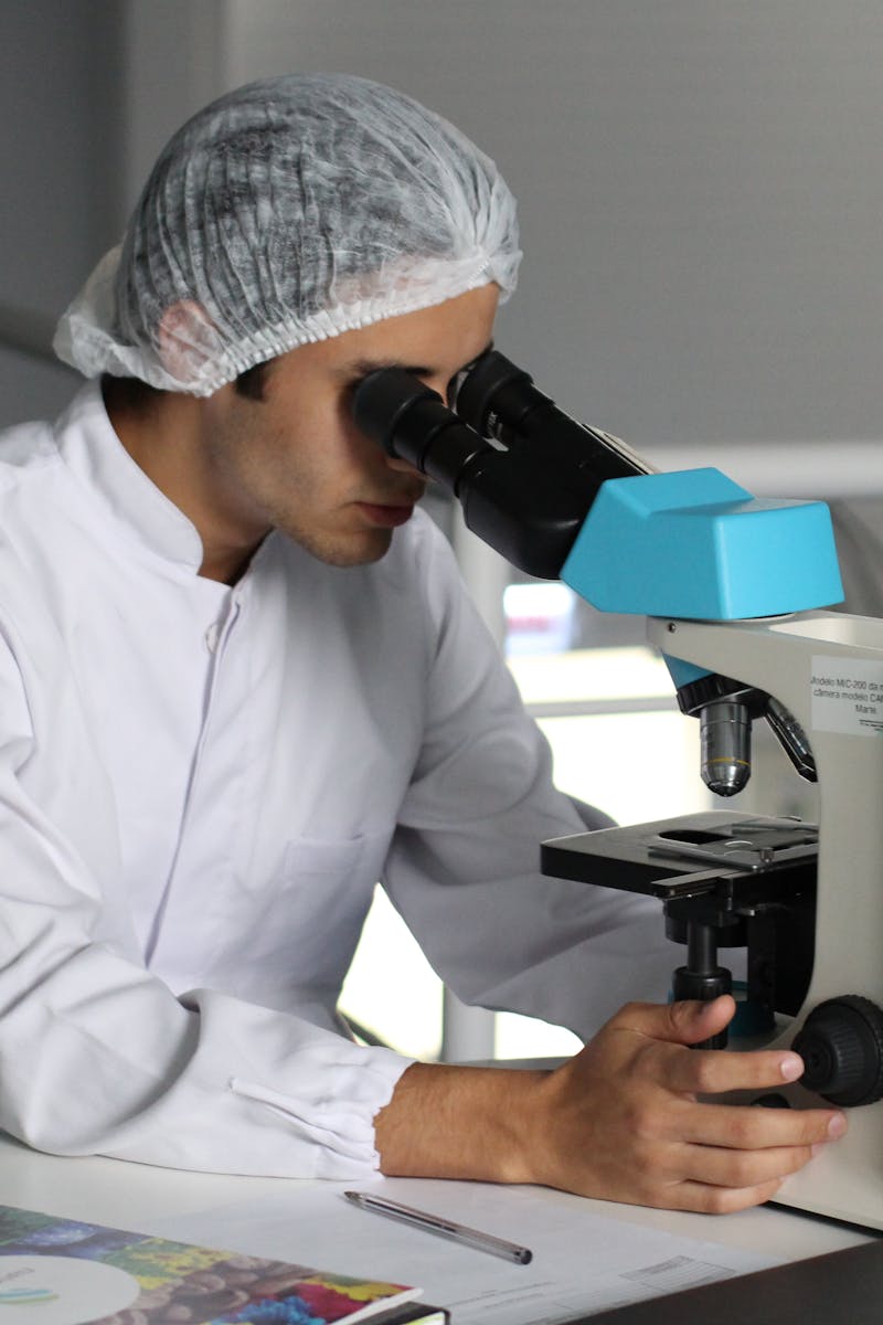 Scientist in a lab coat using a microscope to conduct research, focusing on healthcare improvements.